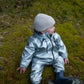 A toddler in a Waterproof Baby/Kid Clothing Set in silver from MellowConceptStore sits on a moss-covered rock, looking off to the side.