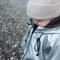A child dressed in warm, Waterproof Baby/Kid Clothing Set - Silver from MellowConceptStore, including a hat and a hooded coat made of merino wool, is looking downwards against a background of small stones or gravel.
