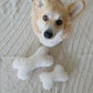 A corgi standing next to a white Natural Sheepskin Dog Toy Bone from Mellow Pet Store, a sustainable dog toy.
